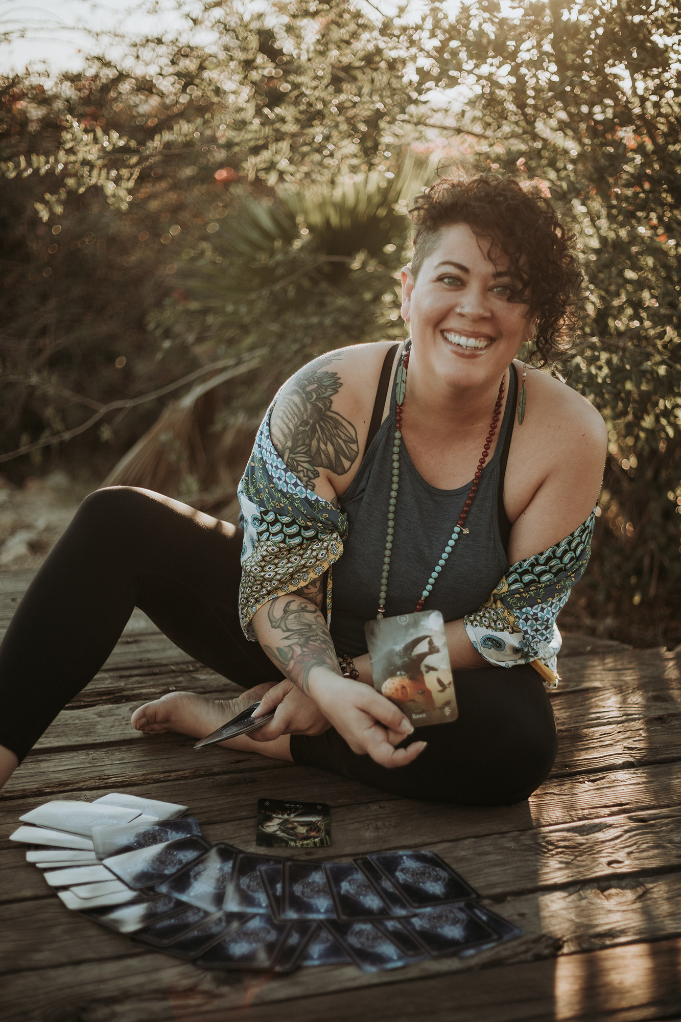 Image of Vivianna Severance sitting on a deck, outside, with tarot cards spread in front of her and one in her hand